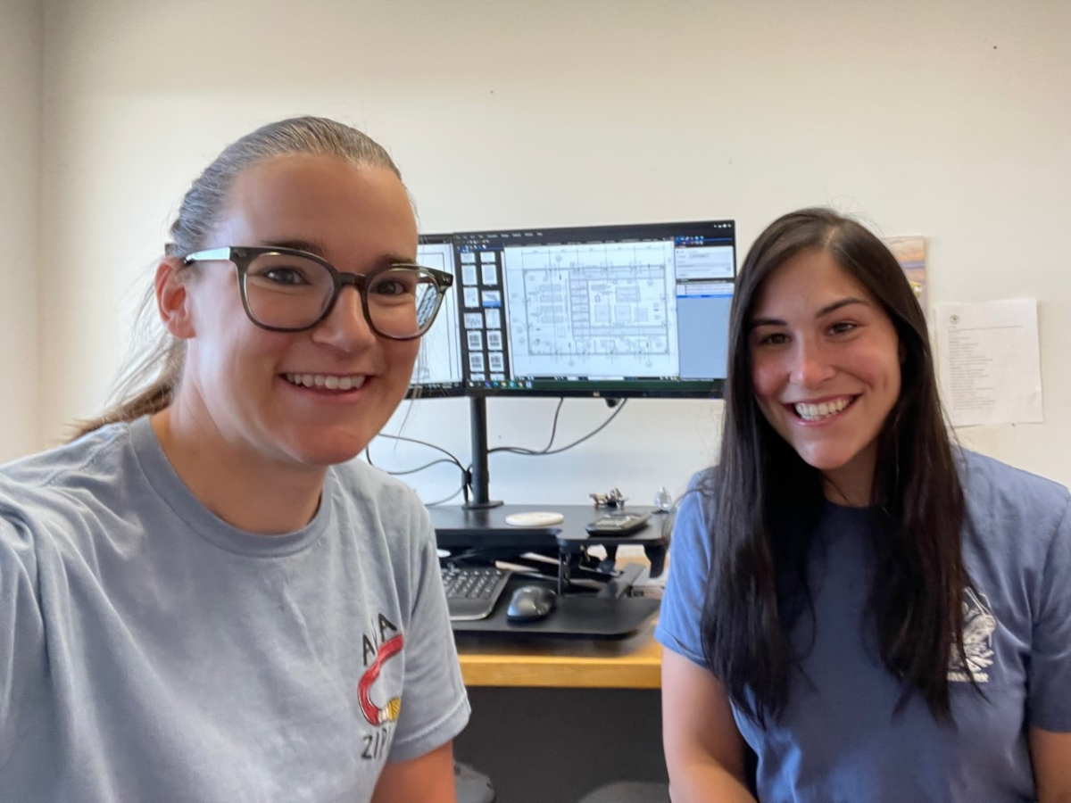 Showing mentorship: Author Katelyn Wager, left, smiles in her office with her mentee, Allison Stephens, right. A computer screen is in the background. 