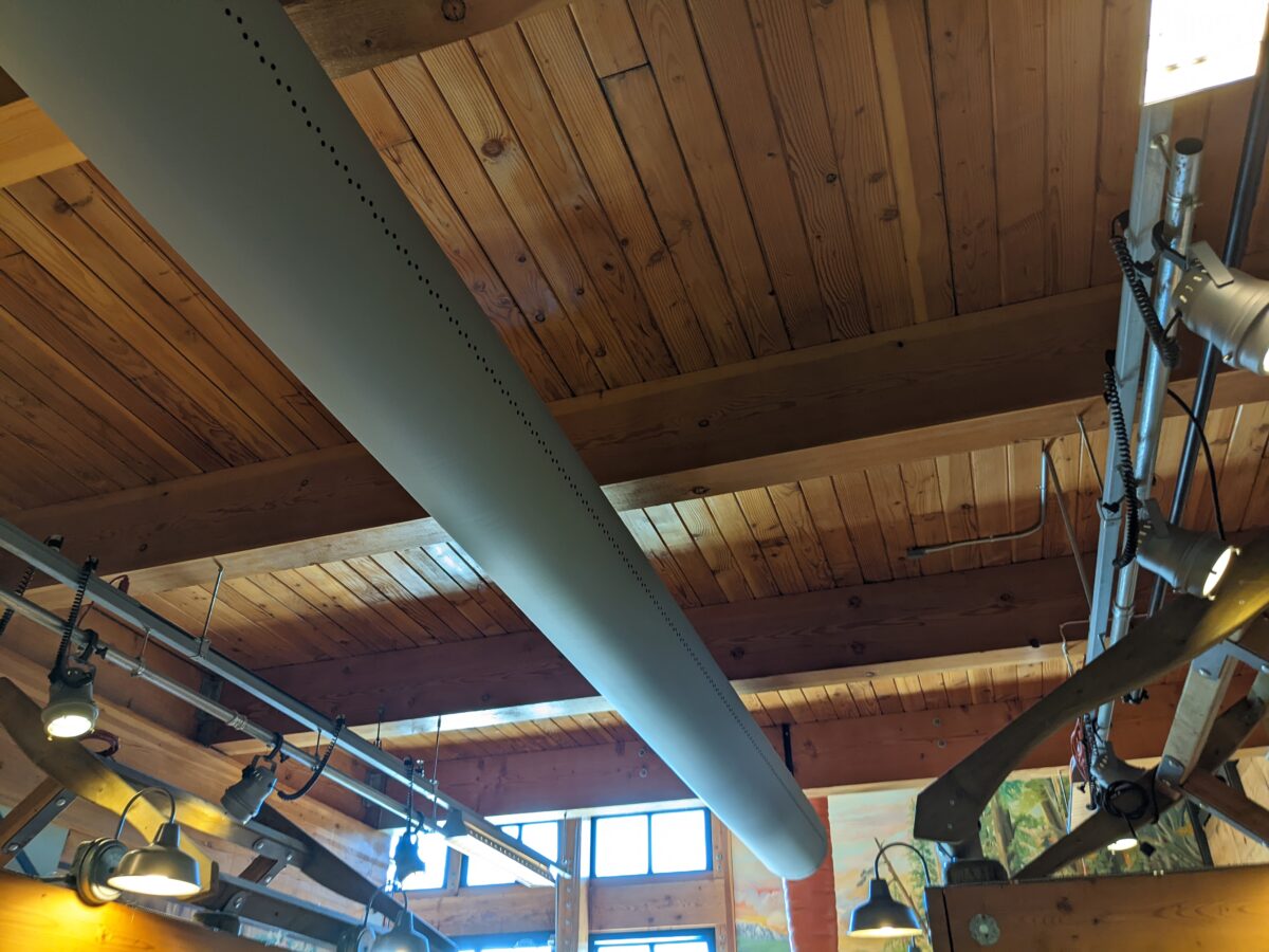 A photograph taken from below shows a pale colored fabric duct running along a finished wooden plank ceiling.