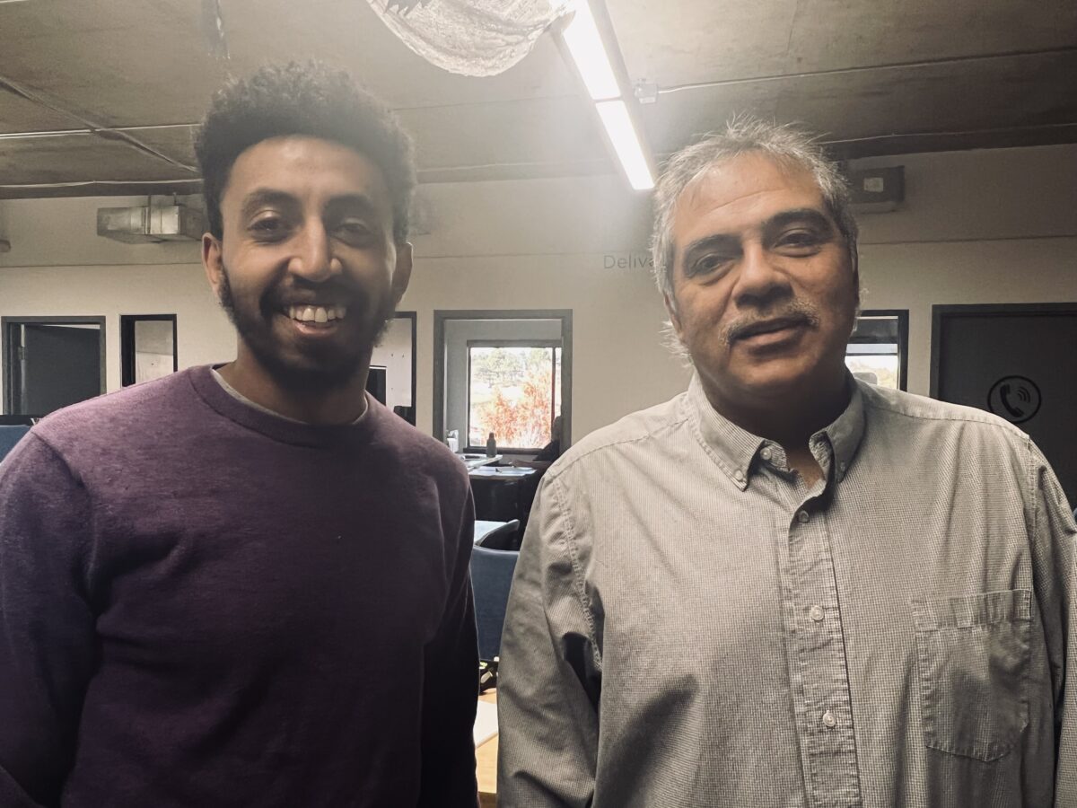 Abraham Meshesha, left, wearing a purple crew-neck sweater, smiles with his mentor, Adrian Vigil, right, wearing a light grey button up shirt. They are in the EVstudio office, in the architecture department.