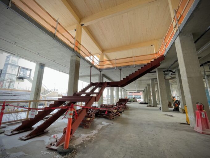 A red steel-frame staircase is shown inside a a room that is under construction.
