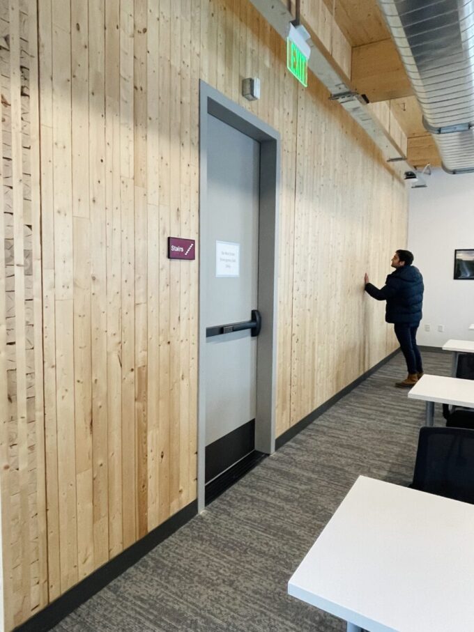 A person leans on and inspects the CLT wall panels, in the background of the focus of the picture, which is a door to the stairwell.