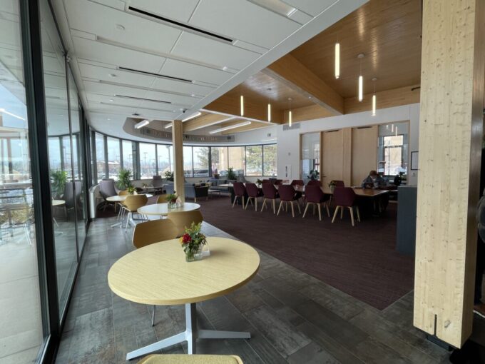 Tables, chairs, and a curved bank of windows are shown inside the Burwell Center.