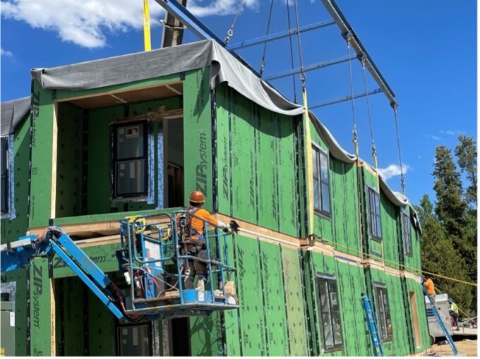 A construction worker in a cherry picker is up close to align a module being set.