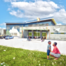 Exterior rendering of TLC Early Learning Collaborative - features grey fiber cement panels and blue and green stucco that echoes the surrounding mountains. A butterfly roof adds a unique and exciting element for students and staff alike.