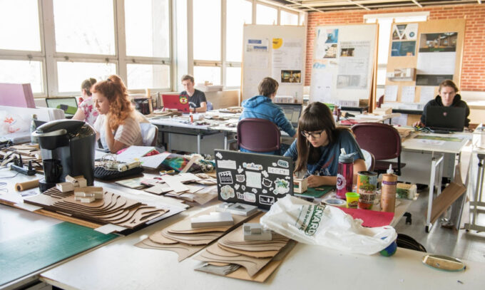 Architecture students working with laser-cut wood models and laptops in a university design studio