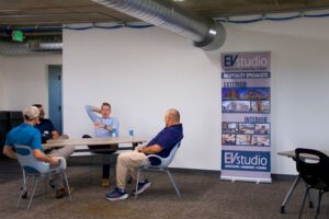Four attendees in conversation beside an EVstudio Hospitality Specialists banner during the happy hour Caption: The conversation ranged from preconstruction budgeting to weekend plans