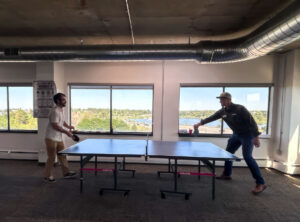 Two happy hour attendees mid-rally at the ping pong table in the EVstudio Denver office Caption: Friendly competition, mostly