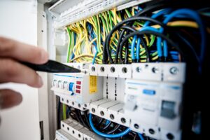 Electrician using a screwdriver on a circuit breaker panel filled with colored wiring.