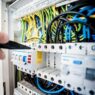 Electrician using a screwdriver on a circuit breaker panel filled with colored wiring.