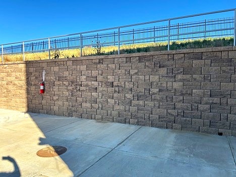 Retaining wall with sidewalk at the base and a railing at the top.